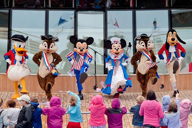 People dressed up in disney costumes perform for a crowd of children.