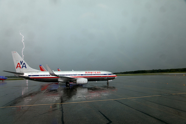 An air plane on a wet runway with lightning in the background.