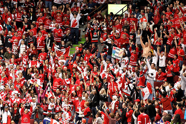 A crowd of people dressed in red and white Canadian jerseys cheer.