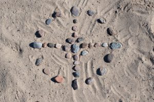 Medicine wheel made of stones on sand with spokes pointing in cardinal directions.