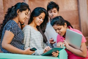 Four Indian students holding devices and looking at one student's iPad. iStock.