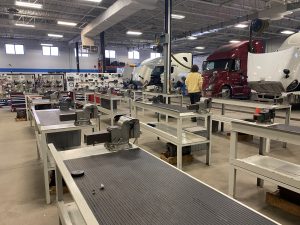 Large trucks with their hoods up, work space benches, in a large room. A student faces the trucks