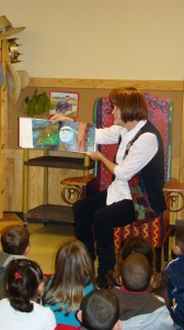 Children sit on the floor around a teacher as she reads to them.