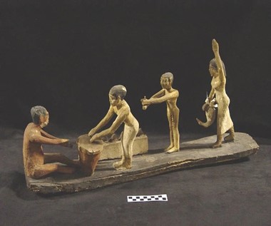 A carving showing three people engaged in work related to brewing beer while a woman on the right with her hand up appears to be in a position of authority