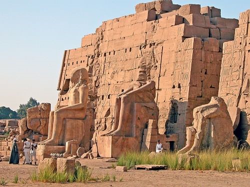 A large temple with giant seated figures and tiny human beings alongside showing the size.