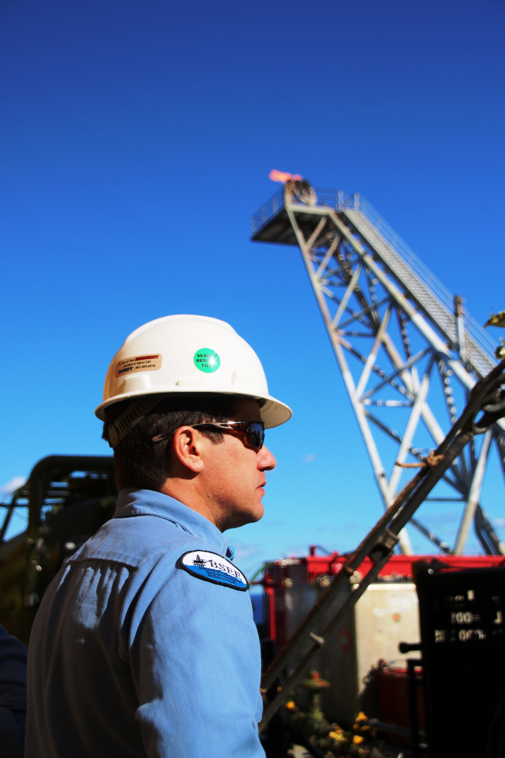Safety Inspector oversees inspections of temporary equipment, while gas is flared in the background at the top of a flare stack on Front Runner.