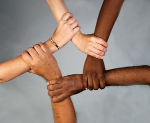 The right hand of five different people holding onto another's right forearm to create the shape of a circle