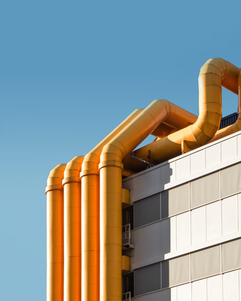 Photo of many yellow pipes down the side of a grey building.