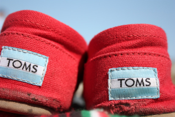 Well-worn heels and back sides of a pair of red Toms Shoes, with a light-blue and white tag saying TOMS