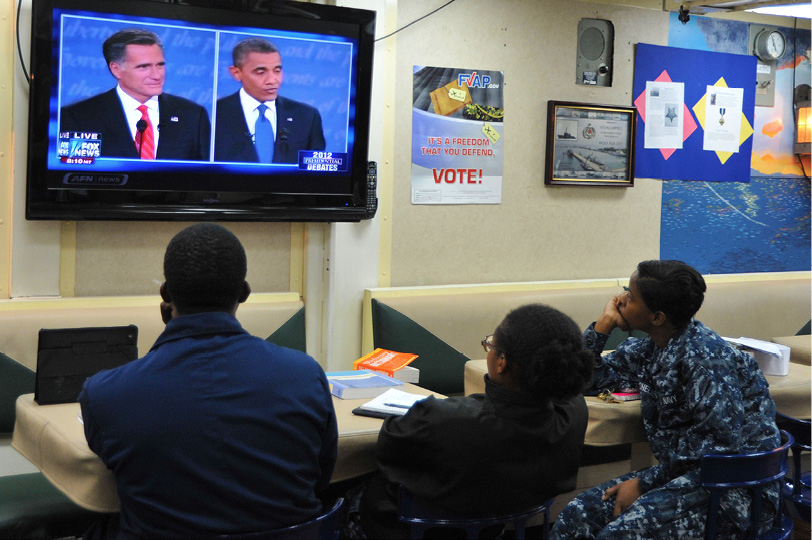 Two men and a woman in sailor uniform watching on TV the U.S. Presidential debate between candidates Barack Obama and Mitt Romney in 2012.