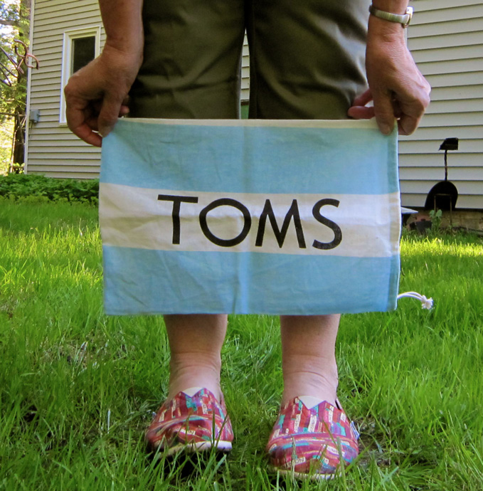 Person holding a small blue and white cloth banner that reads "TOMS".