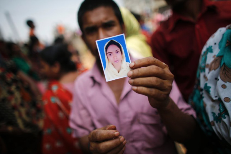 A man in a crowd holds up a passport photo of a woman.
