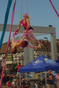 Two arial acrobats perform above a crowd.