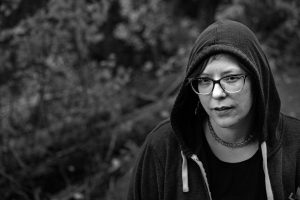 a black and white image of a non-binary person in a dark hoodie