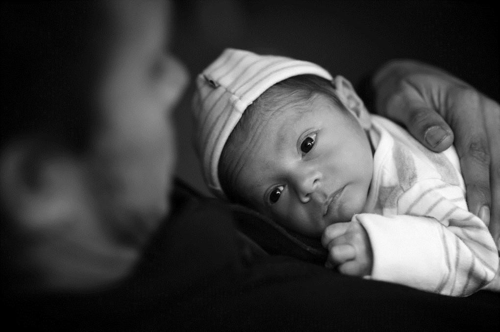 image of a newborn baby lying on an adults chest and appearing to gaze up at the adult's face