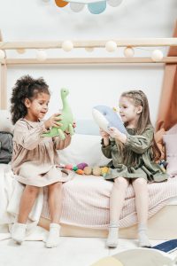 An image of two children sitting on a bed playing with a stuffed dinosaur and whale