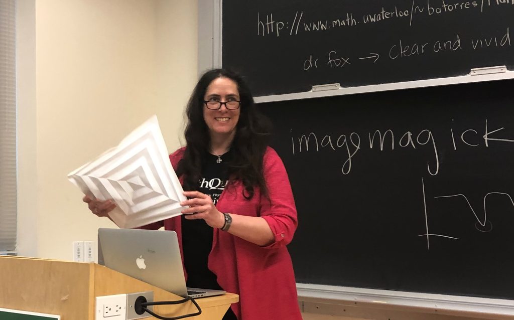 person holding a visual aid, in front of a blackboard