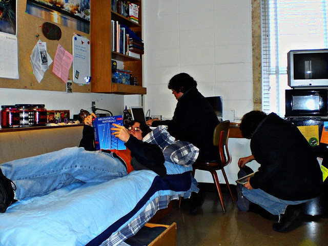 A student tries to study in a dorm room while friends read and hang out.