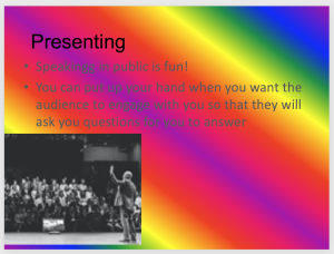Example PowerPoint slide with multicolour rainbow background. In the bottom left-hand corner is a black and white image of a person with their hand up addressing an audience. Black header reading "Presenting" and grey font in a bulleted list reading: Speakingg in public is fun! You can put up your hand when you want the audience to engage with you so that they will ask you questions for you to answer.