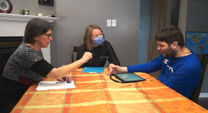 Capture d'écran de la vidéo "Consultation en ergothérapie à domicile". Léo, Mme Lacroix et Francine, l'ergothérapeute, sont assis à la table à manger et discutent ensemble.