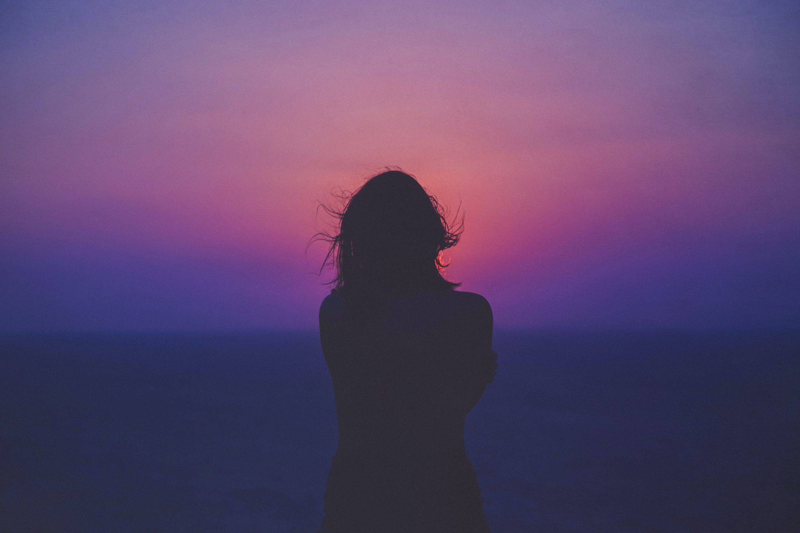 silhouetted figure with long hair against a purple sunset.
