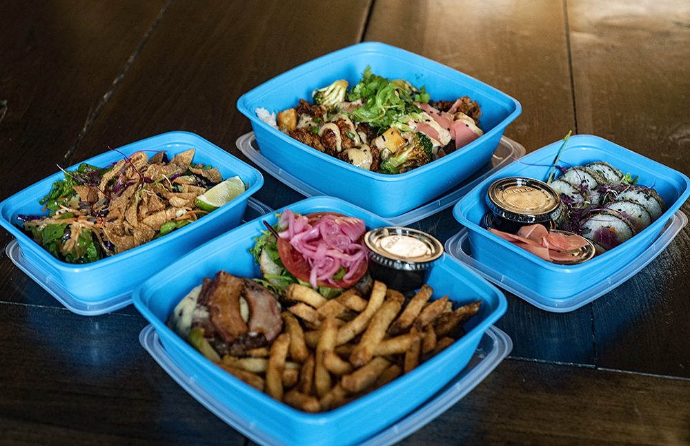 Photo of 4 blue takeout containers with hamburger and French fries, sushi, and two different salad bowls.