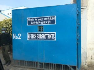 Large entry gate with solid blue surface and the sign Hi-Tech Surfactants in English at centre and a sign in Hindi above it