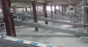 A series of narrow metal conveyer ramps on a diagonal from lower right, beginning in the machines pictured in Photo 4, to upper left. Blue sachets are spaced out on the conveyer.