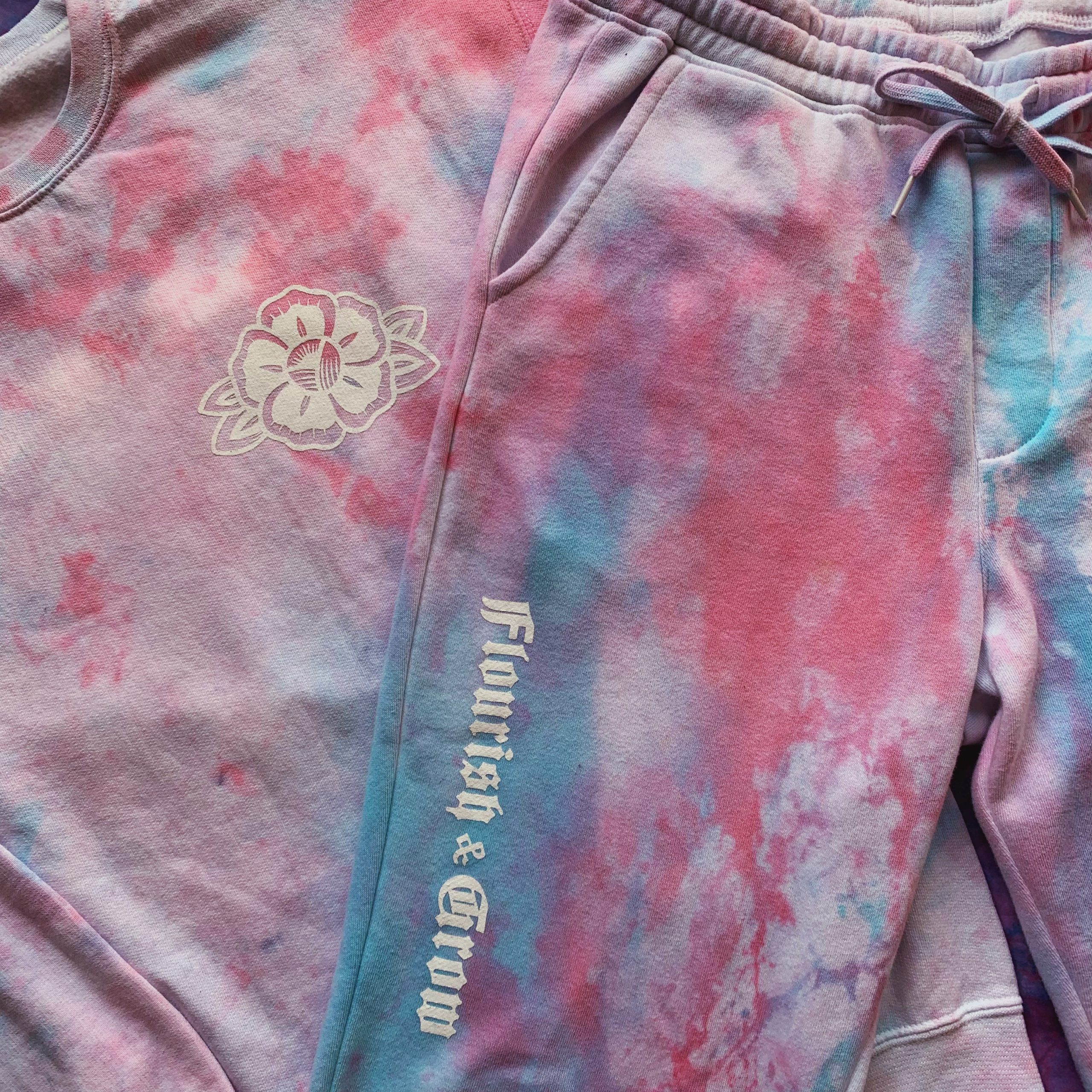 Photo of pink and blue tie-dye sweatshirt and sweatpants with a white flower and the words “Flourish & Grow.”