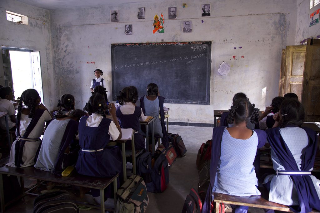 Students in a classroom facing a blackboard. See image description.