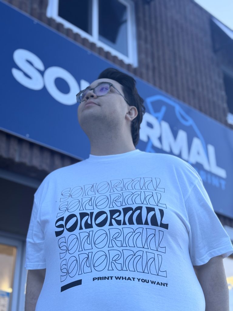 Man with black hair and glasses wearing white SoNormal T-shirt.