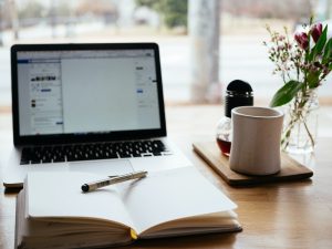 a laptop, coffee, book and pen sit on a table