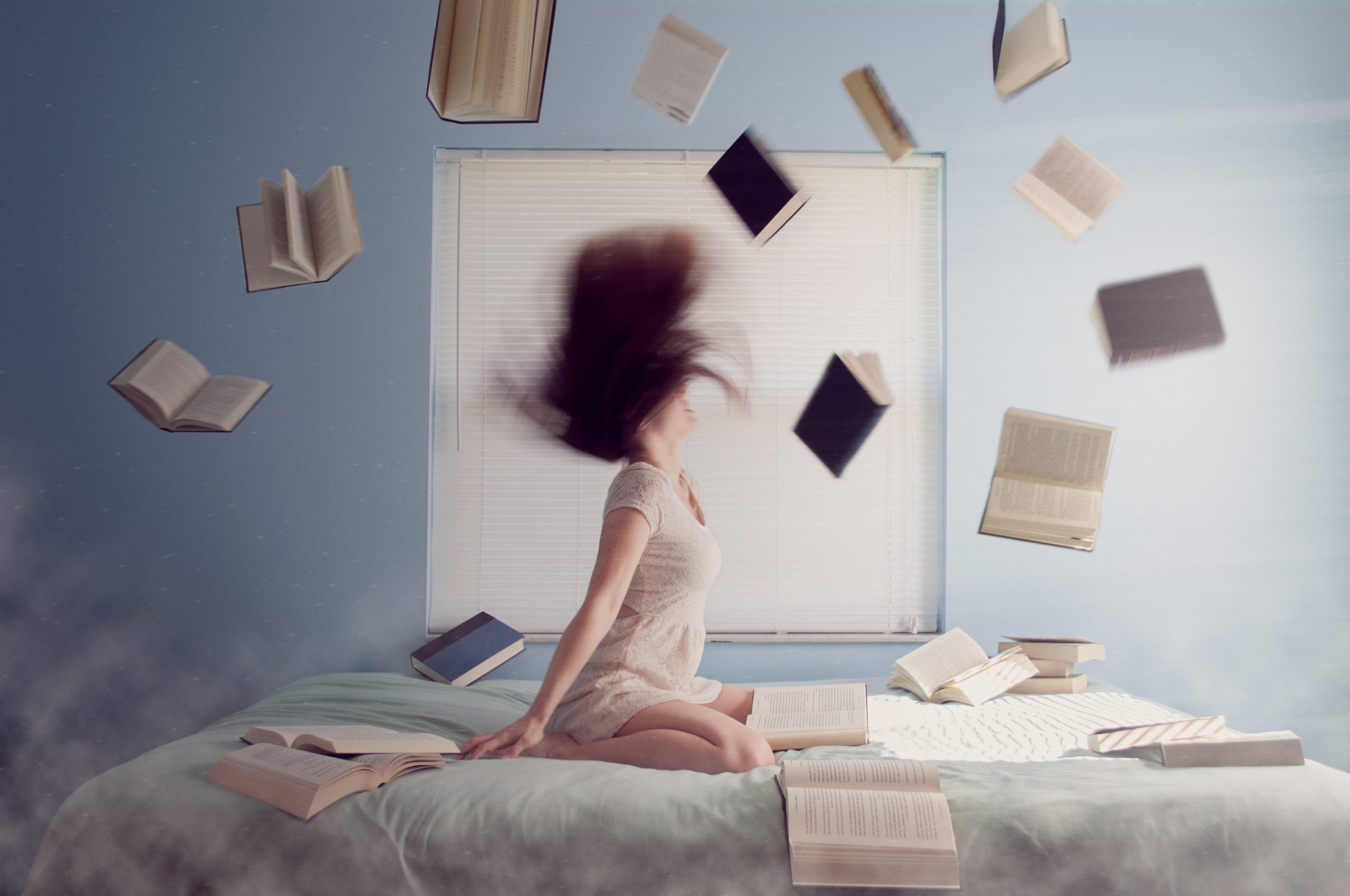 Woman sitting on a bed with books flying in the air.