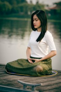Woman meditating on wooden dock during daytime.