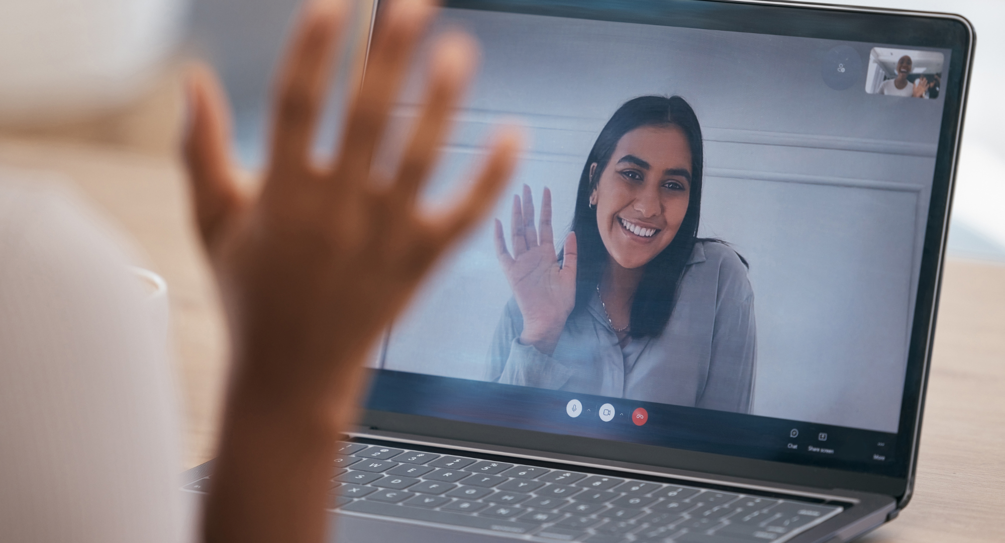 A photo of two people video calling. One person is sitting at a desk the other is pictured on a laptop.