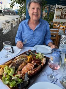 A man sitting at a table with drinks and a lobster dinner.