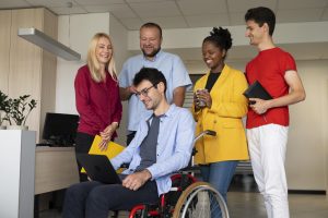 5 employees in an office, one in a wheelchair, smiling and conversing.
