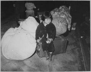 A_young_evacuee_of_Japanese_ancestry_waits_with_the_family_baggage_before_leaving_by_bus_for_an_assembly_center..._-_NARA_-_539959