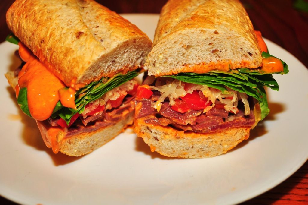 Sandwich cut in half is displayed with ingredients such as lettuch, tomatoes, peppers, and sauce.