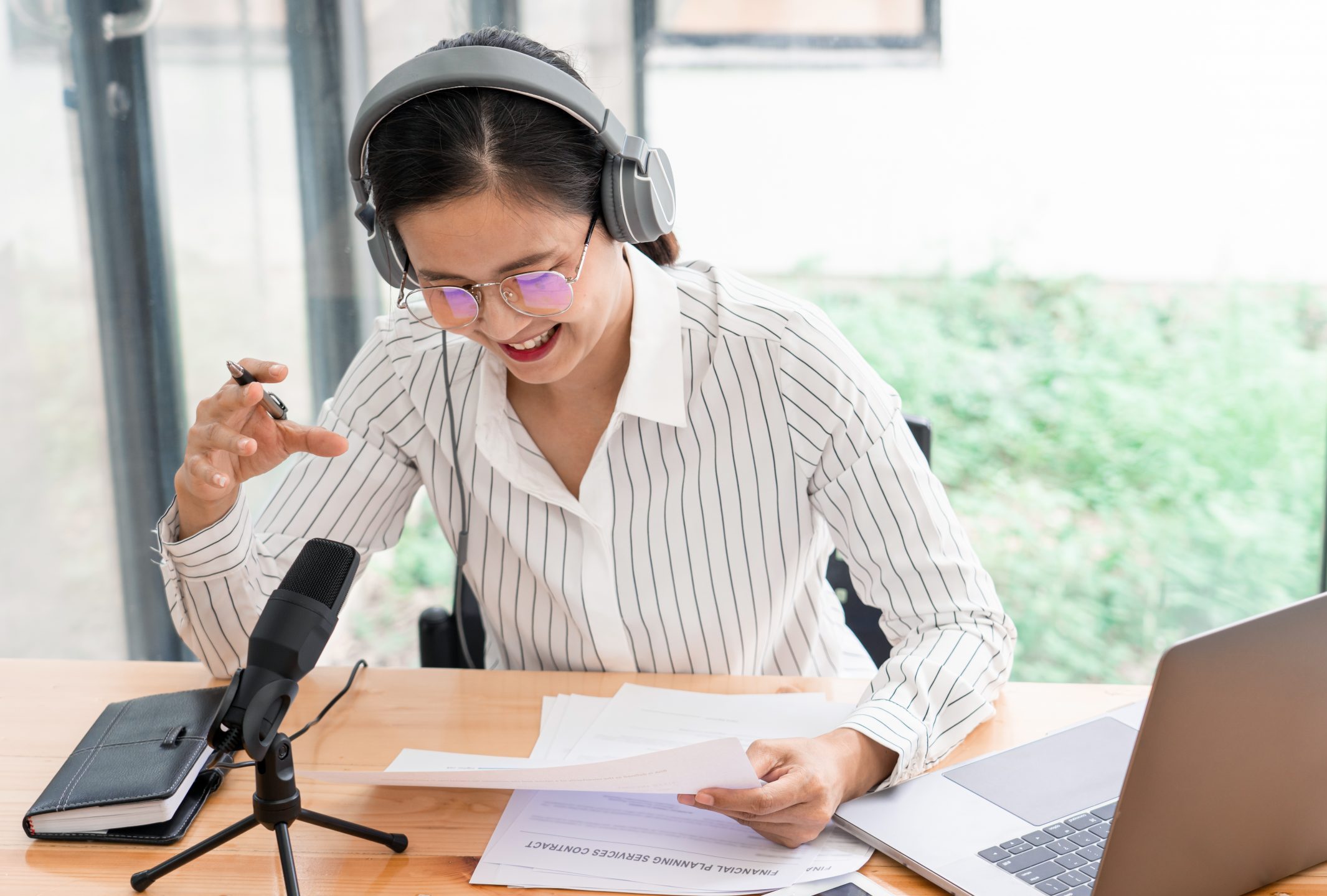 Asian women podcaster recording online talk show at studio using headphones, professional microphone and computer laptop on table.