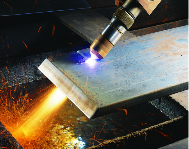 A torch cutting metal is pictured. Bright, white colored plasma is shown near the tip of a torch where it is contacting the metal.