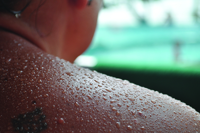 A person’s shoulder and neck are shown and their skin is covered in beads of liquid.