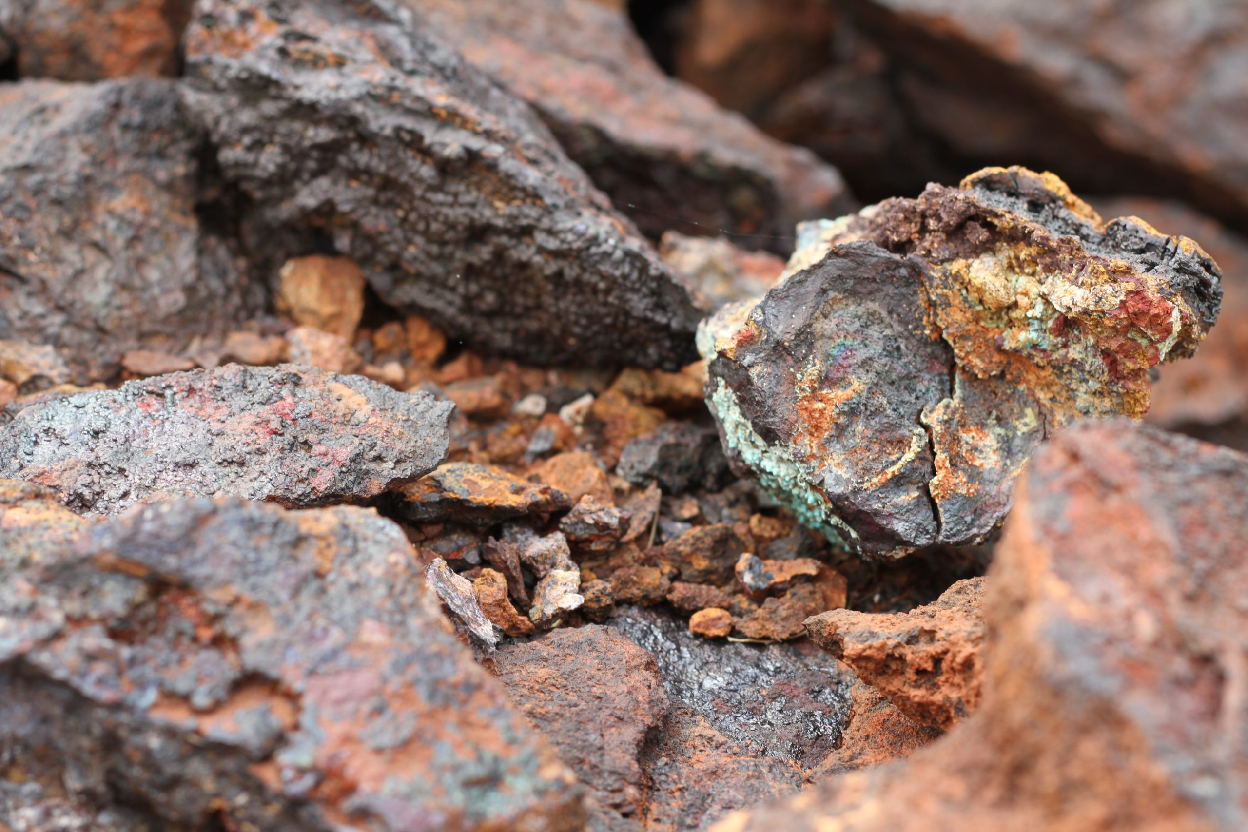 Dark grey solid rock of ore with colours of orange, brown, green and yellow is pictured.