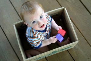 young child sitting in a box holding two plastic block pieces