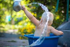 young child sitting in a water basin outside and they are throwing water in the air