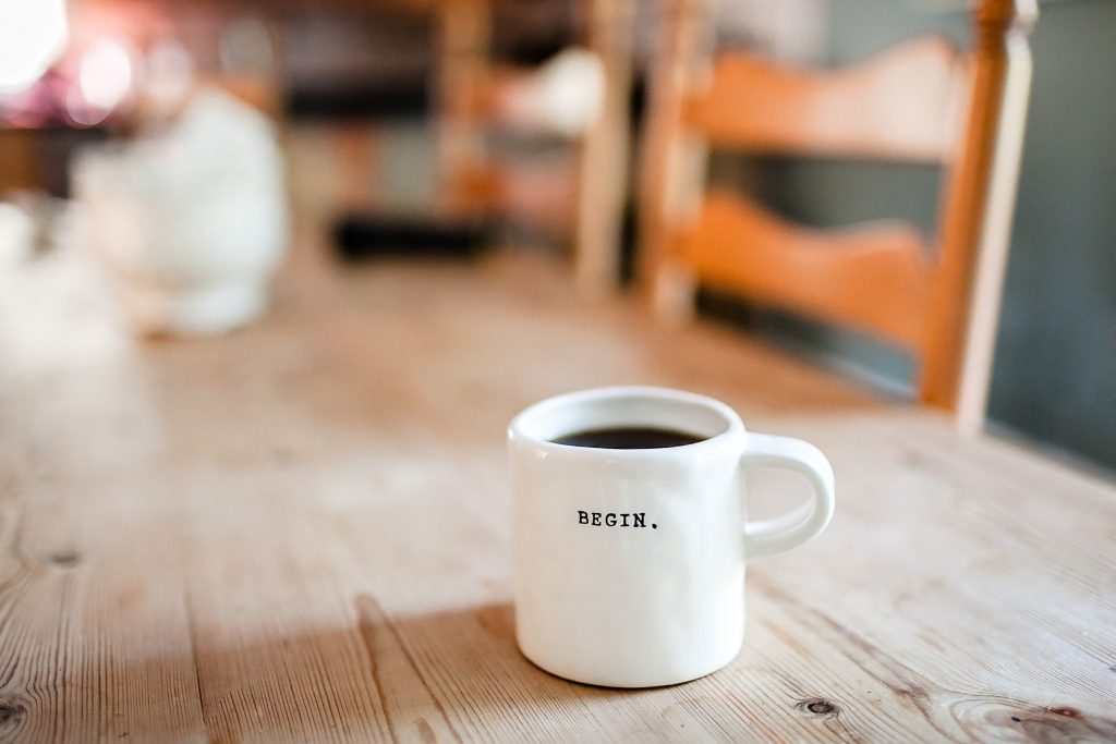 white mug on a coffee table, the mug has the word begin on it