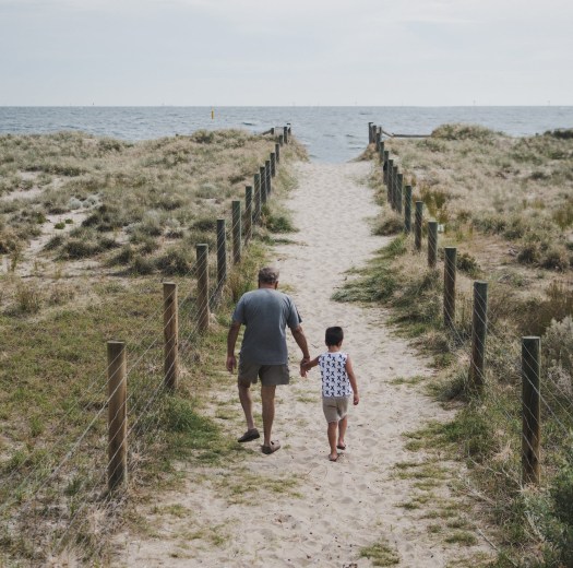 man and boy walking across pathway heading to beach