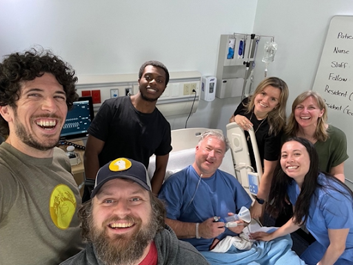 Seven members of the film team posing at bedside in nursing lab.
