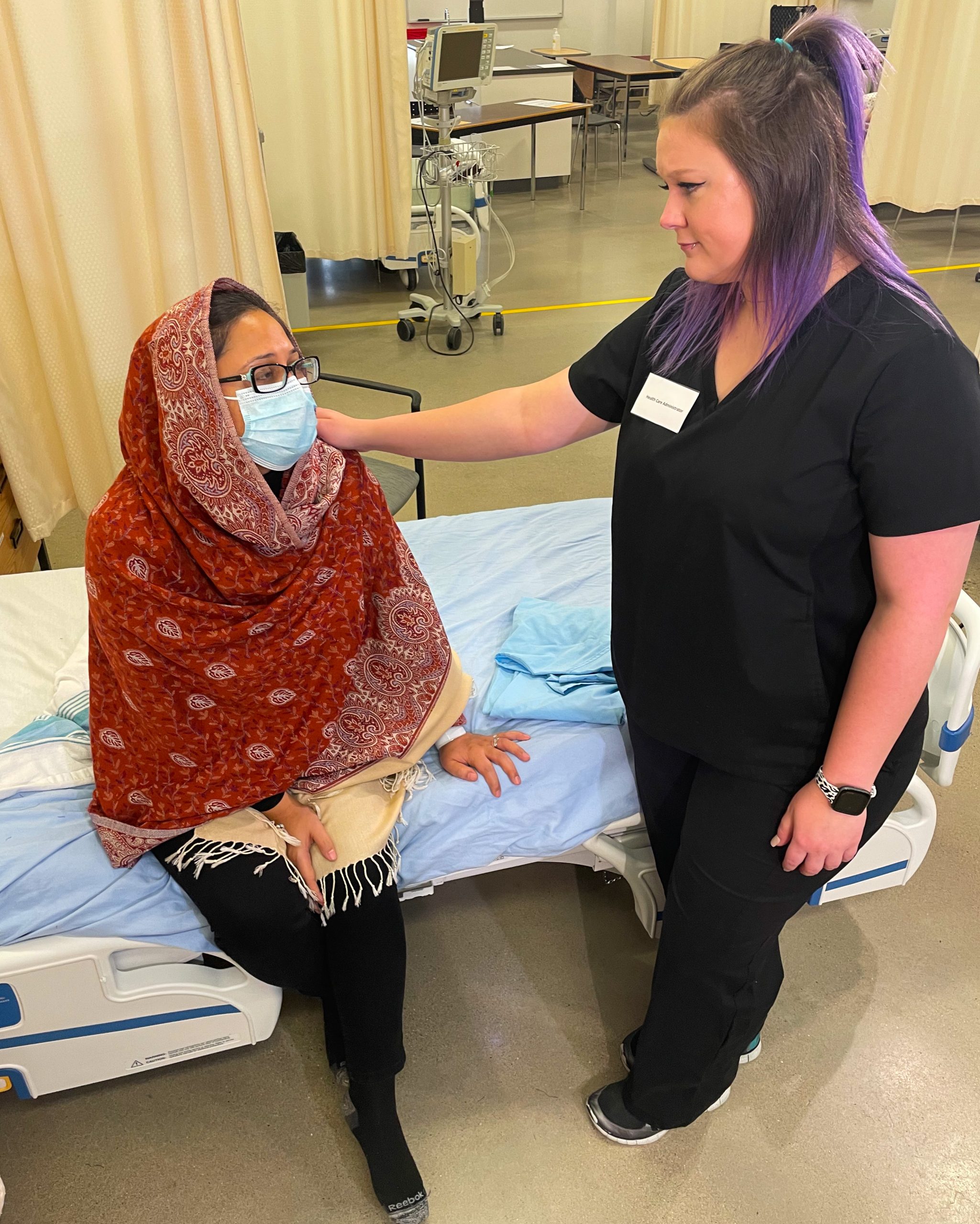 Health Care Administrator comforting a client sitting on a hospital bed with therapeutic touch.