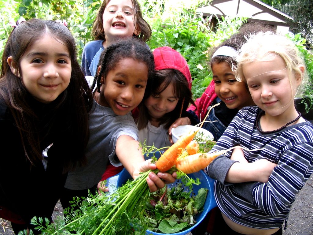 A group of kids holding fresh vegetables to the camera.